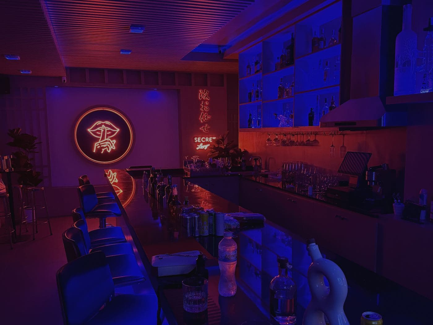 Барная стойка Secret Lounge в Паттайе в красном и синем свете, неоновый логотип за бутылками